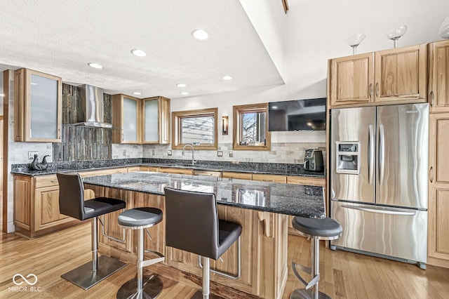 kitchen with a breakfast bar, wall chimney range hood, stainless steel refrigerator with ice dispenser, and a sink