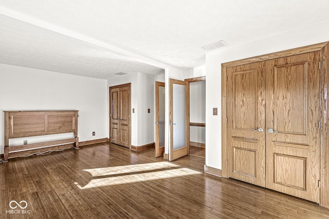 unfurnished bedroom with a textured ceiling, wood finished floors, visible vents, and baseboards