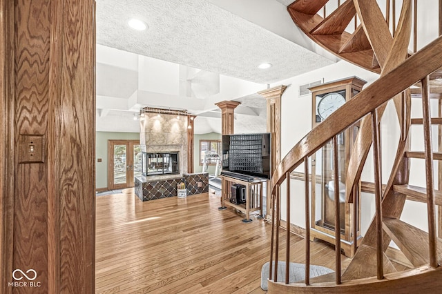 stairway with a textured ceiling, wood finished floors, visible vents, and ornate columns