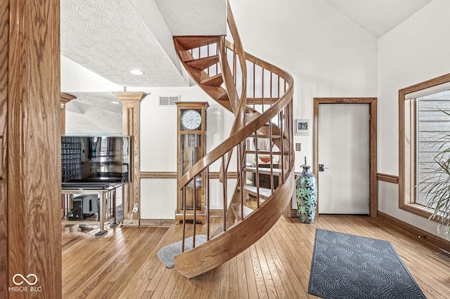 foyer featuring lofted ceiling, wood-type flooring, visible vents, stairway, and a textured ceiling