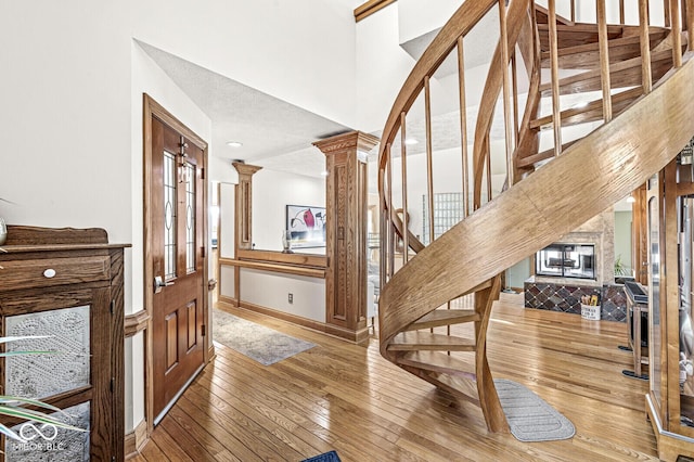 entryway featuring decorative columns, a towering ceiling, hardwood / wood-style floors, baseboards, and stairs