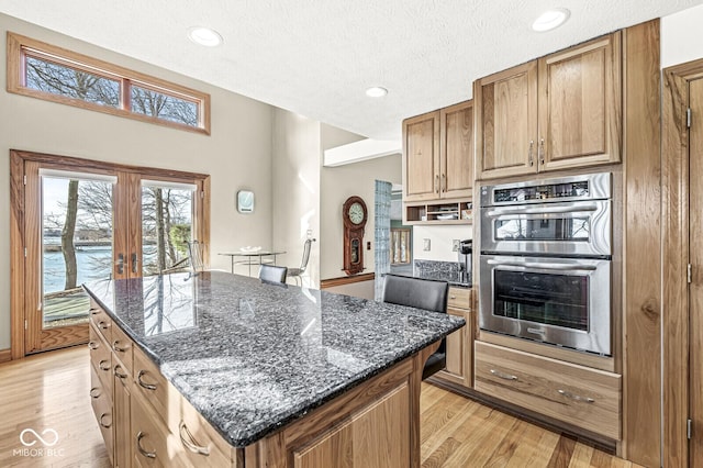 kitchen with double oven, a center island, french doors, and light wood-style flooring