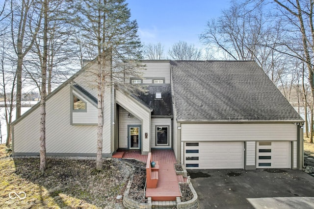 view of front facade with driveway, an attached garage, a deck, and roof with shingles