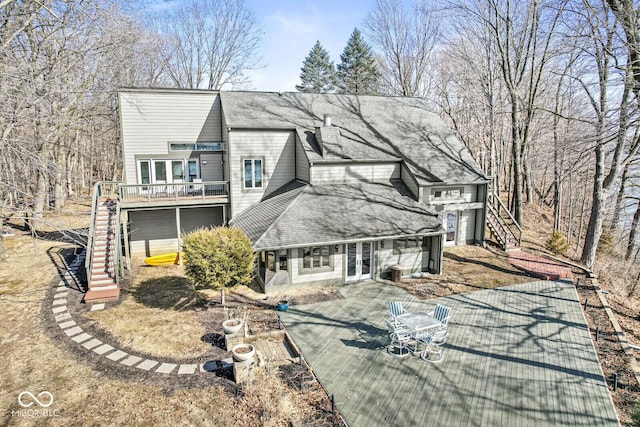 view of front of house with stairs, french doors, a deck, and roof with shingles