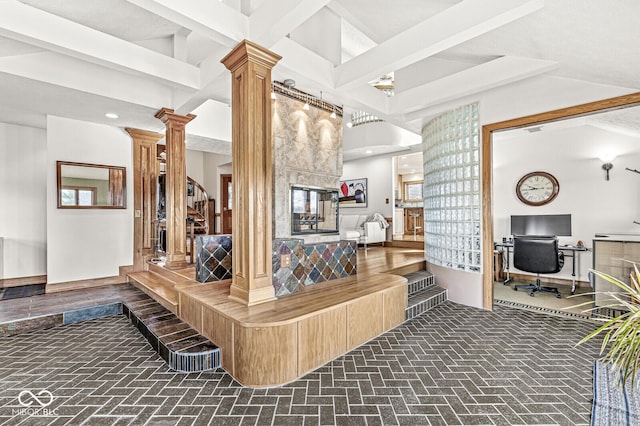 interior space with brick floor, beam ceiling, a fireplace, decorative columns, and a towering ceiling