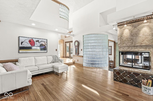 living area featuring a towering ceiling, a textured ceiling, track lighting, a tile fireplace, and hardwood / wood-style floors