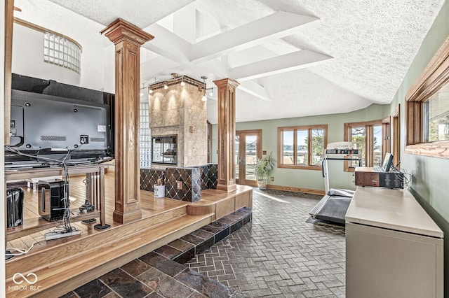 interior space with a textured ceiling, a tiled fireplace, decorative columns, and baseboards