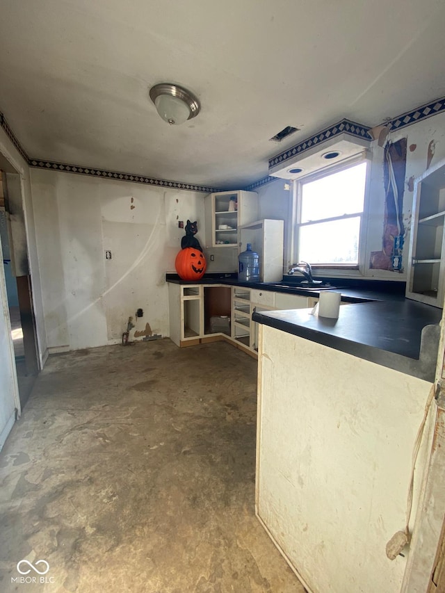 kitchen featuring dark countertops, unfinished concrete floors, open shelves, and a sink