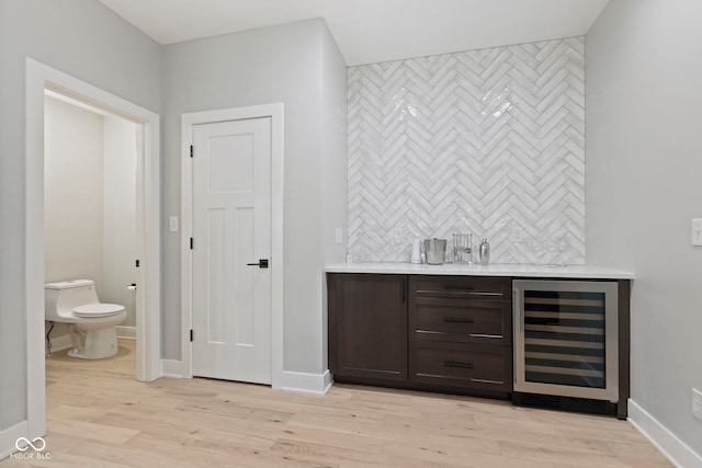 bar featuring light wood-style floors, beverage cooler, baseboards, and decorative backsplash