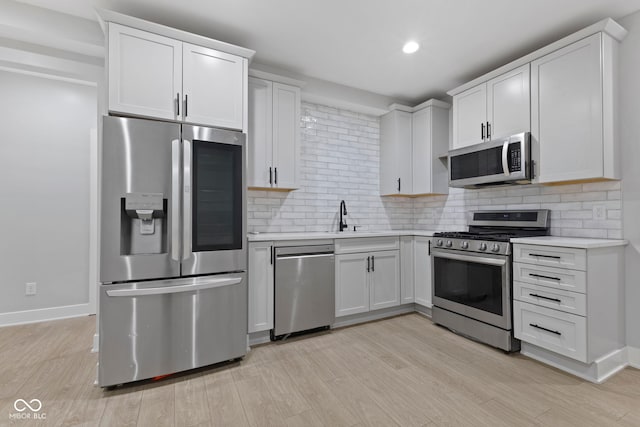 kitchen with appliances with stainless steel finishes, light countertops, light wood-style flooring, and backsplash