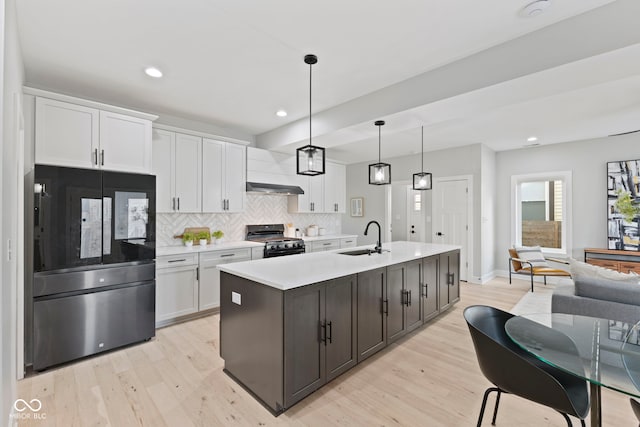 kitchen featuring light countertops, refrigerator with glass door, gas stove, white cabinets, and a sink