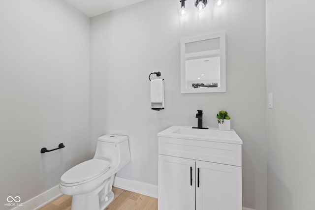 half bath with wood finished floors, vanity, toilet, and baseboards