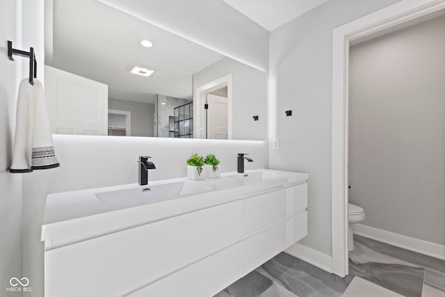 bathroom with double vanity, toilet, a sink, a shower stall, and baseboards