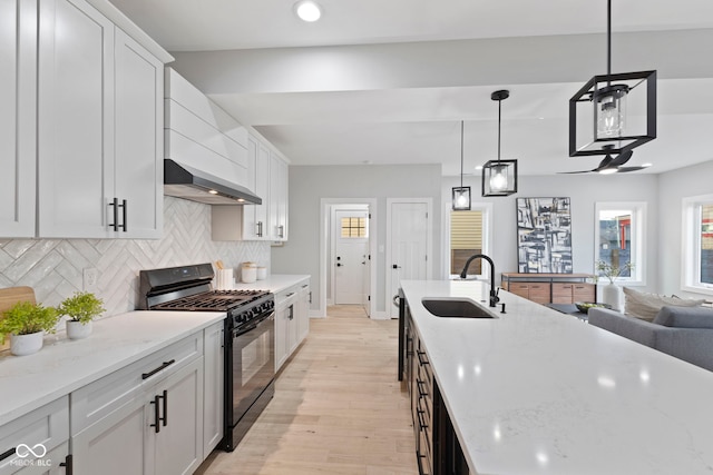 kitchen featuring tasteful backsplash, black range with gas stovetop, light wood-style floors, a sink, and wall chimney exhaust hood