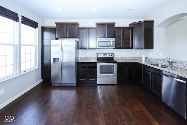 kitchen featuring light stone counters, appliances with stainless steel finishes, dark wood-type flooring, and a sink