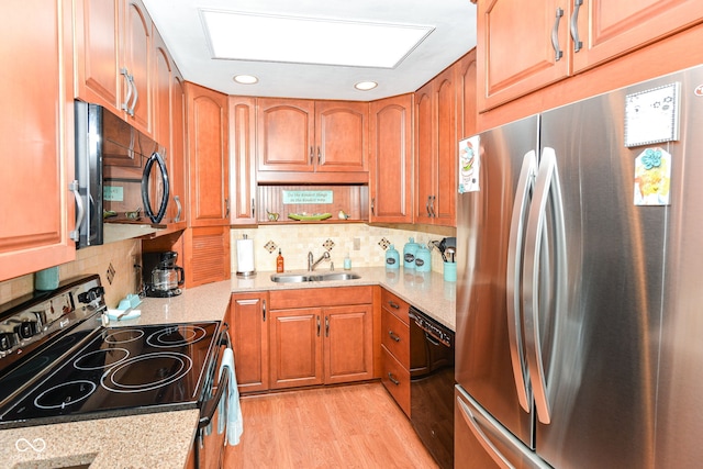 kitchen featuring black appliances, light wood-type flooring, a sink, and decorative backsplash