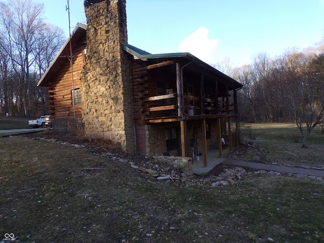 view of side of property with a chimney, log siding, a deck, and a patio