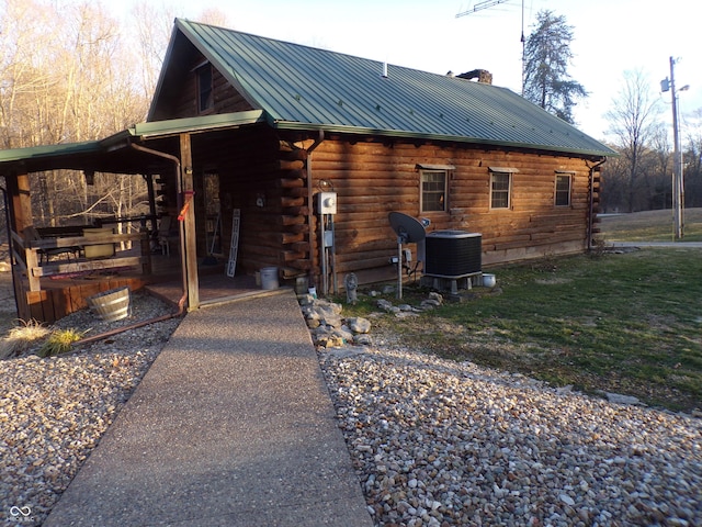 exterior space featuring metal roof, cooling unit, a lawn, log exterior, and a chimney