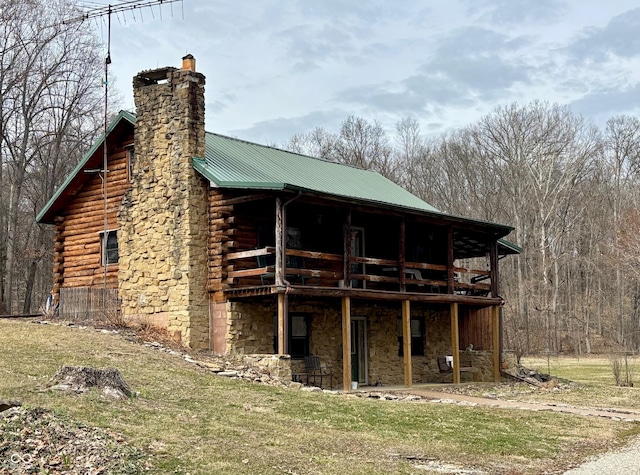 exterior space with stone siding, metal roof, a chimney, and log siding