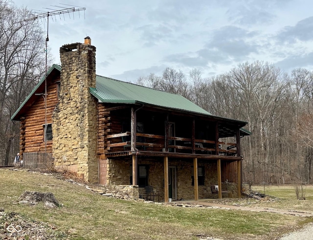 exterior space featuring stone siding, metal roof, a chimney, and log siding