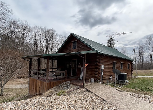 view of front facade featuring covered porch, cooling unit, metal roof, and log exterior