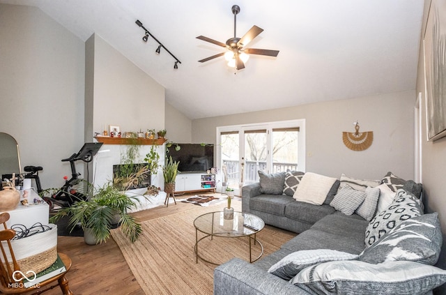 living room featuring lofted ceiling, a tile fireplace, wood finished floors, a ceiling fan, and rail lighting