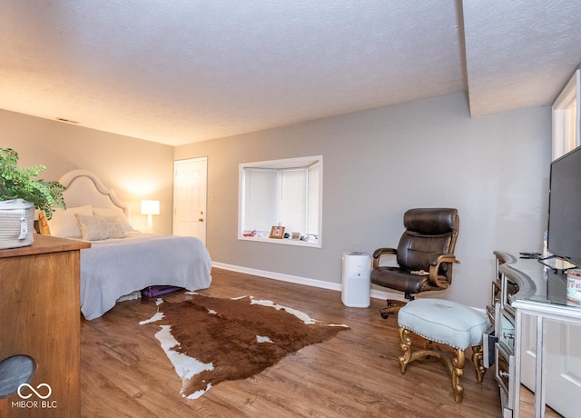 bedroom featuring multiple windows, a textured ceiling, baseboards, and wood finished floors