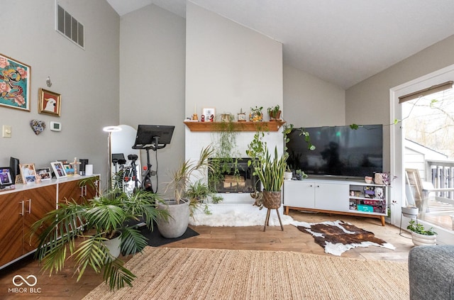 living area with visible vents, vaulted ceiling, a fireplace, and wood finished floors