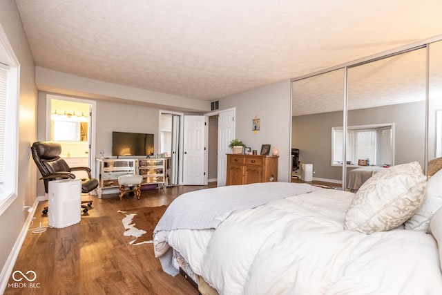 bedroom with baseboards, a textured ceiling, visible vents, and wood finished floors