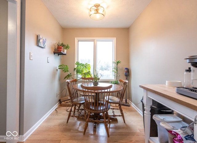 dining room featuring baseboards, a textured ceiling, and light wood-style floors