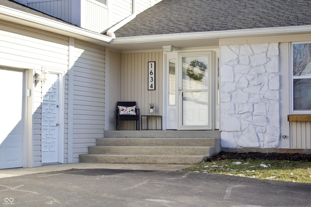 entrance to property featuring a shingled roof, stone siding, and a garage