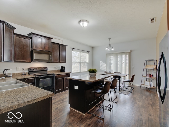 kitchen featuring a kitchen island, dark wood-style flooring, dark brown cabinets, black appliances, and a sink