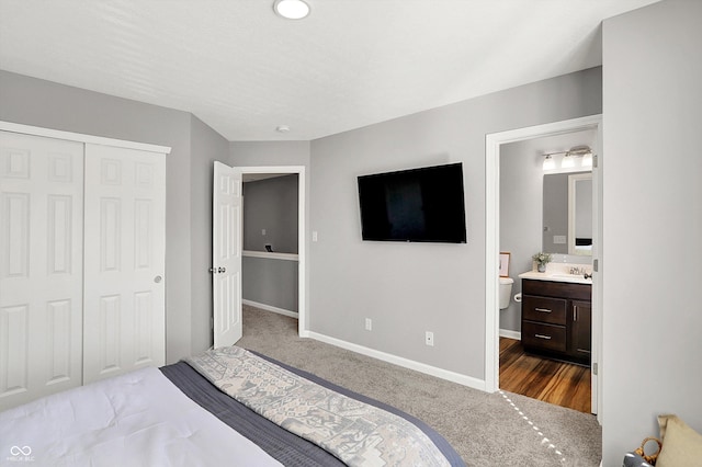 bedroom with baseboards, dark carpet, ensuite bathroom, a closet, and a sink