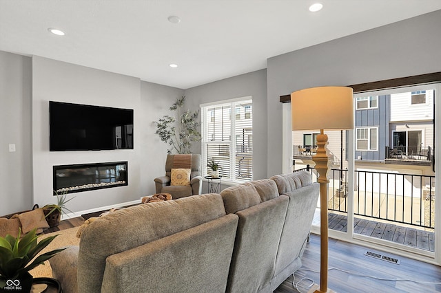 living room with recessed lighting, visible vents, wood finished floors, and a glass covered fireplace