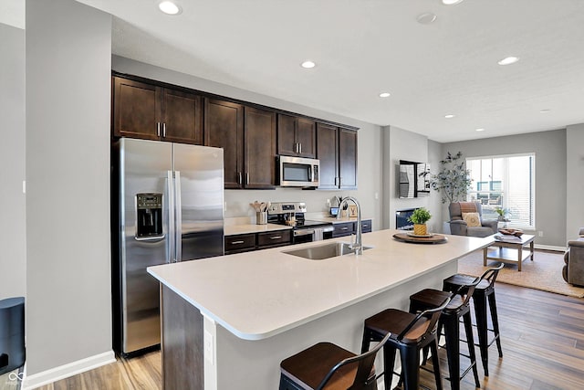 kitchen with a sink, open floor plan, stainless steel appliances, dark brown cabinetry, and light wood finished floors