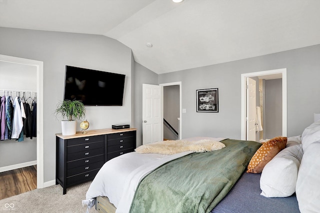 bedroom with a walk in closet, light carpet, lofted ceiling, a closet, and baseboards