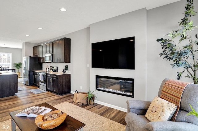 living area featuring recessed lighting, baseboards, a glass covered fireplace, and wood finished floors