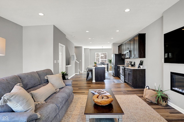 living area with recessed lighting, baseboards, a glass covered fireplace, and wood finished floors