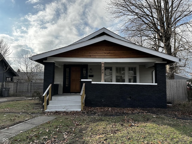 bungalow-style home featuring fence, a porch, and brick siding