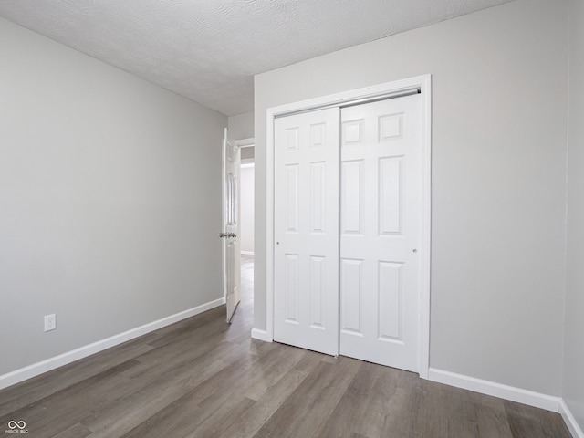 unfurnished bedroom with a closet, a textured ceiling, baseboards, and wood finished floors