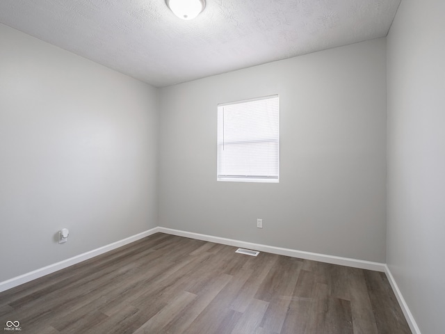 spare room featuring visible vents, a textured ceiling, baseboards, and wood finished floors