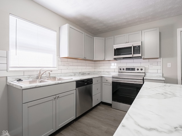 kitchen with appliances with stainless steel finishes, wood finished floors, a sink, a textured ceiling, and backsplash