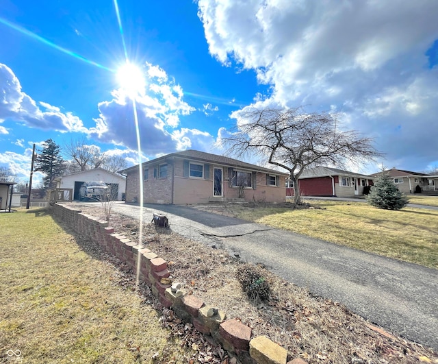 single story home featuring a front yard, brick siding, an outdoor structure, and driveway