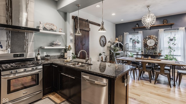 kitchen with open shelves, stainless steel appliances, a barn door, a sink, and wall chimney range hood