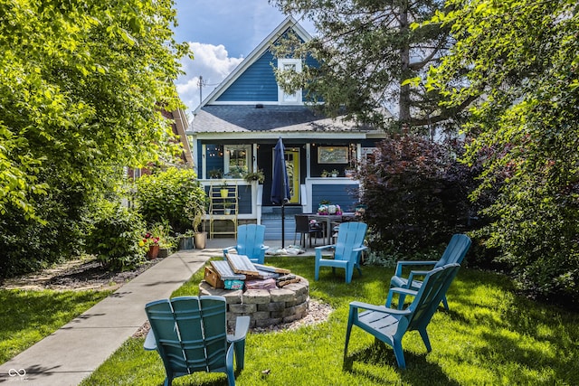 view of front of house featuring roof with shingles, an outdoor fire pit, and a front lawn