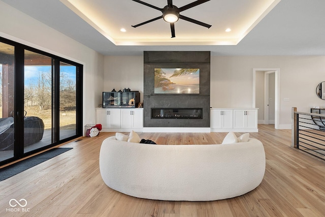 living area with a tray ceiling, light wood-style flooring, and a fireplace