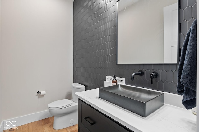 bathroom featuring vanity, wood finished floors, toilet, baseboards, and tasteful backsplash