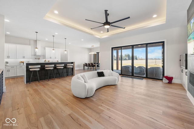 living area featuring light wood-style floors, a ceiling fan, a tray ceiling, and recessed lighting