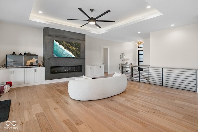 living area featuring recessed lighting, a tray ceiling, ceiling fan, and light wood-style floors