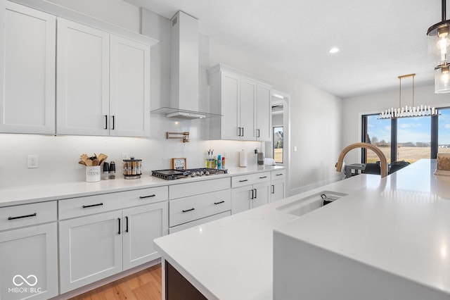 kitchen featuring white cabinets, a sink, stainless steel gas cooktop, wall chimney exhaust hood, and pendant lighting